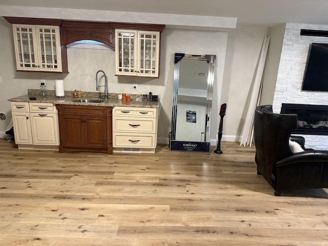 kitchen featuring light stone countertops, a sink, a stone fireplace, light wood-style flooring, and glass insert cabinets