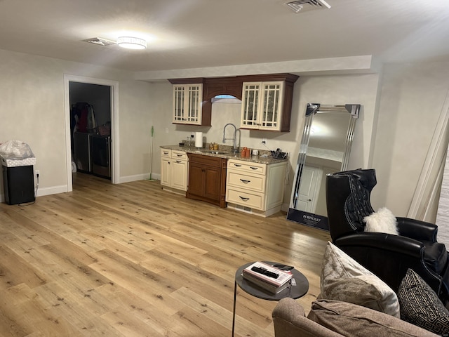 kitchen with visible vents, a sink, baseboards, light wood finished floors, and glass insert cabinets