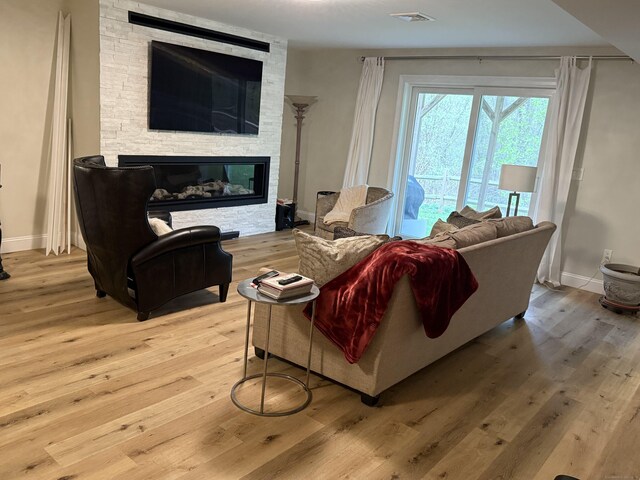 living room featuring visible vents, baseboards, a stone fireplace, and light wood-type flooring