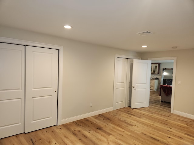 unfurnished bedroom featuring visible vents, baseboards, multiple closets, and light wood-type flooring