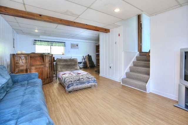 living area with a drop ceiling, a decorative wall, wood finished floors, and stairway