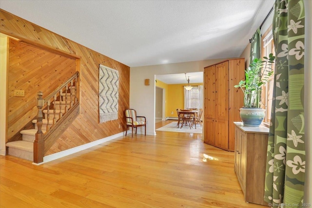 interior space featuring light wood finished floors, wood walls, stairs, and baseboards