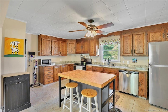 kitchen with brown cabinetry, light tile patterned floors, appliances with stainless steel finishes, and a sink