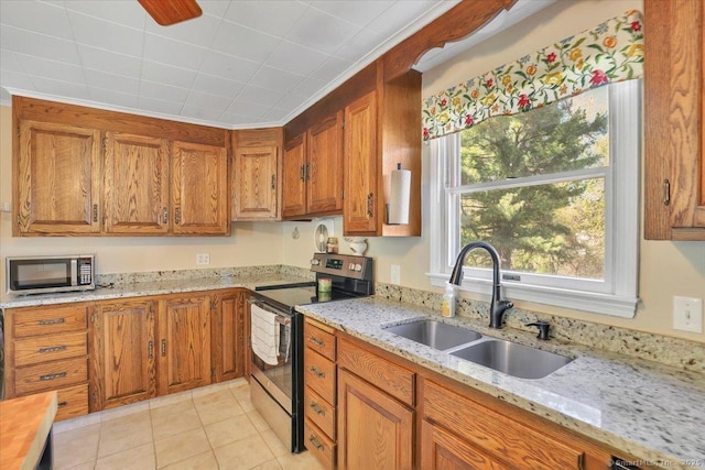 kitchen with a sink, brown cabinetry, stainless steel appliances, and light tile patterned floors
