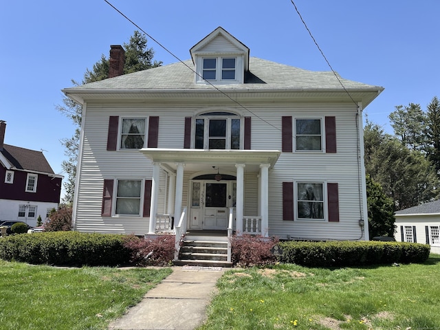 view of front of home featuring covered porch, a chimney, and a front yard