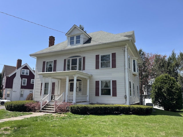 american foursquare style home with a porch, a chimney, and a front yard