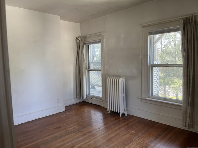 empty room featuring a wealth of natural light, radiator, and hardwood / wood-style floors