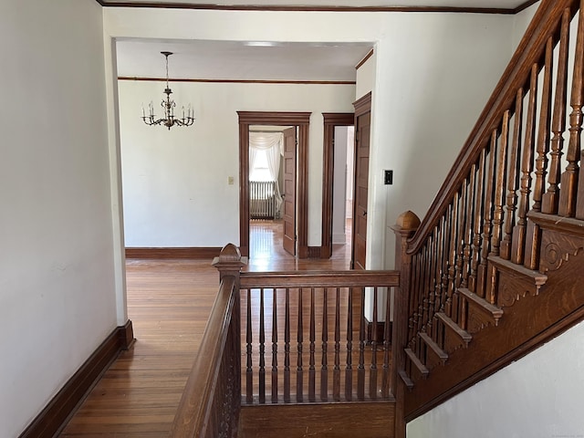 stairs with an inviting chandelier, baseboards, ornamental molding, and hardwood / wood-style floors