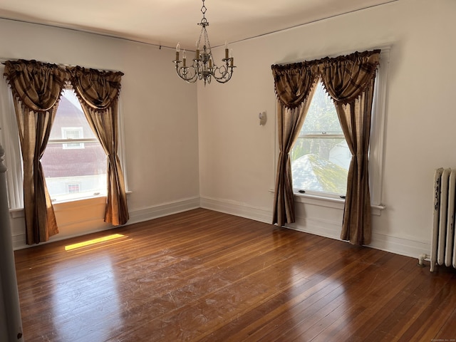 unfurnished room with an inviting chandelier, radiator, baseboards, and dark wood finished floors