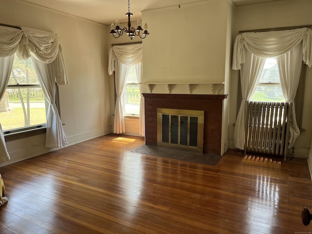 unfurnished living room with an inviting chandelier, baseboards, radiator heating unit, and hardwood / wood-style floors
