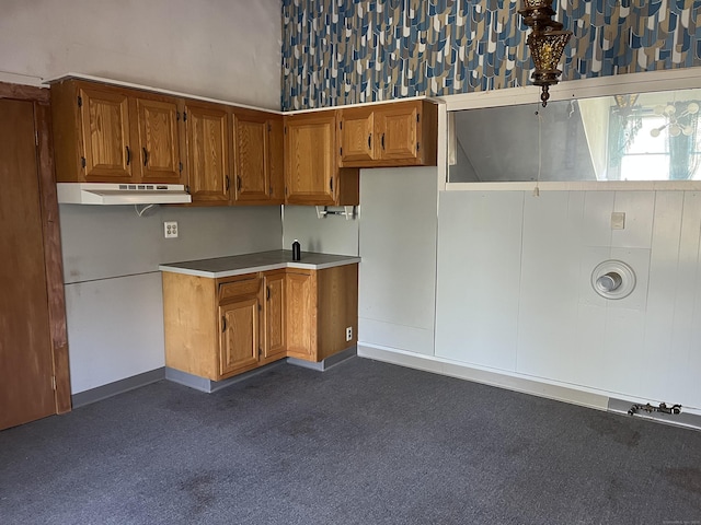 kitchen featuring brown cabinetry, baseboards, dark colored carpet, light countertops, and under cabinet range hood
