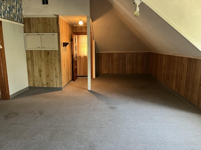 additional living space with carpet flooring, baseboards, wood walls, and lofted ceiling