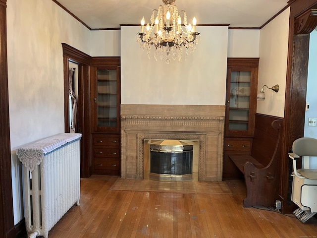 living area with wood-type flooring, ornamental molding, radiator heating unit, and a high end fireplace