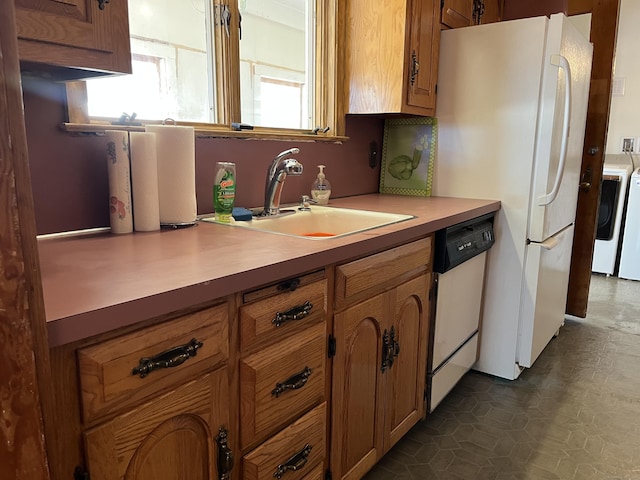 kitchen featuring white appliances, brown cabinets, washing machine and dryer, and a sink