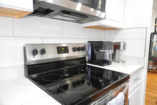kitchen with stainless steel appliances, tasteful backsplash, white cabinets, and light stone countertops