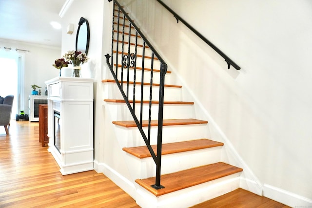 staircase featuring wood finished floors, baseboards, and crown molding
