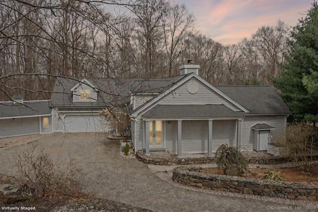 view of front facade with decorative driveway, a chimney, and roof with shingles