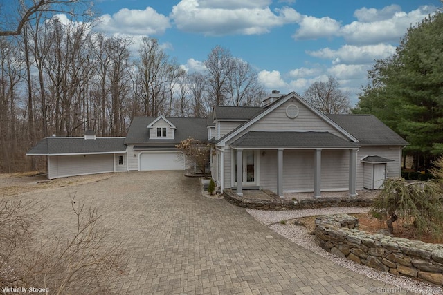 view of front of property featuring a porch, decorative driveway, an attached garage, and a chimney
