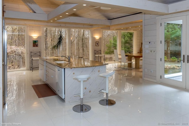 kitchen with white cabinets, light tile patterned flooring, a sink, dishwasher, and an island with sink