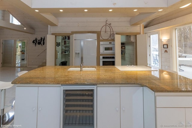 kitchen with wood walls, built in refrigerator, beverage cooler, stone counters, and recessed lighting