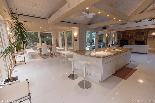 kitchen featuring a kitchen island with sink, an outdoor stone fireplace, wooden ceiling, white cabinets, and open floor plan
