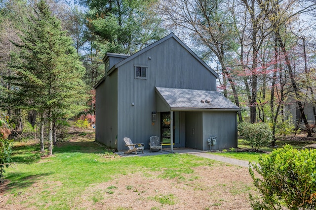 back of property with roof with shingles, a patio, and a yard