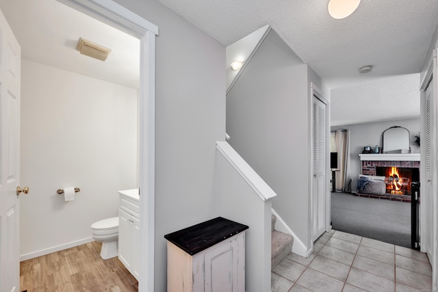 bathroom with a textured ceiling, a fireplace, baseboards, vanity, and toilet