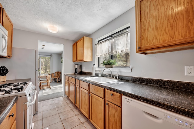 kitchen featuring white appliances, light tile patterned floors, dark countertops, and a sink