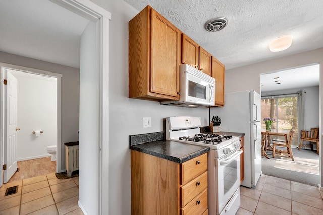 kitchen with visible vents, dark countertops, light tile patterned floors, and white appliances