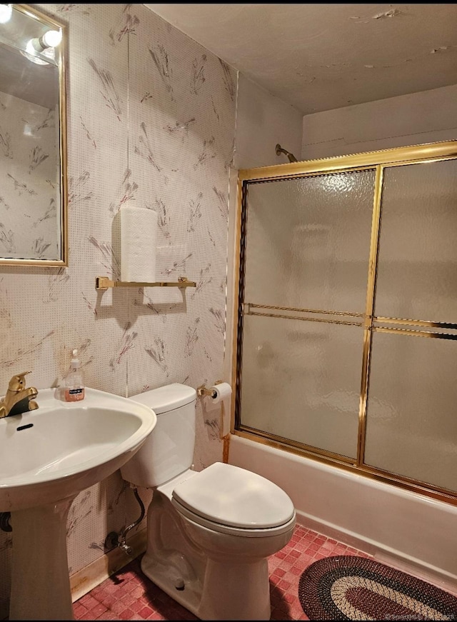 bathroom with bath / shower combo with glass door, toilet, and wallpapered walls