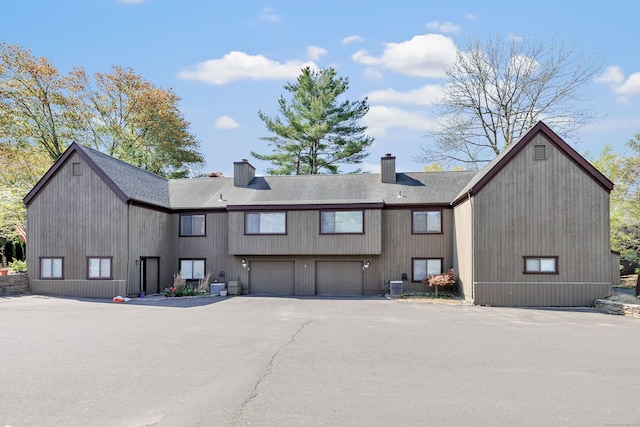 rear view of property with a garage, roof with shingles, driveway, and a chimney