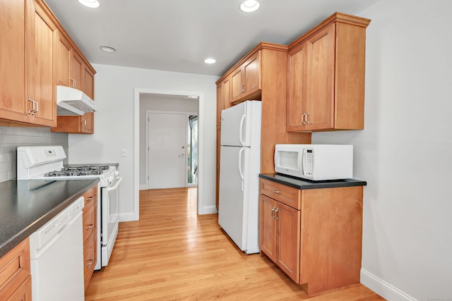 kitchen featuring dark countertops, light wood finished floors, under cabinet range hood, and white appliances