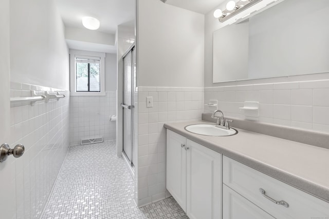 full bath featuring tile walls, a wainscoted wall, a shower stall, and visible vents