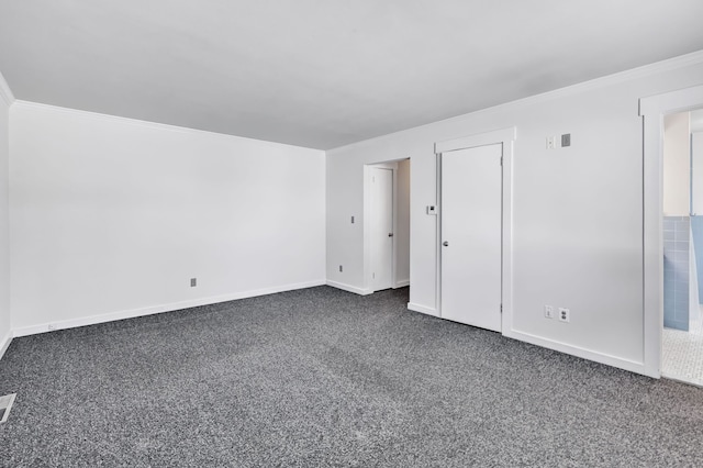 spare room with baseboards, visible vents, ornamental molding, and dark colored carpet