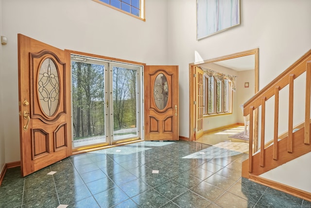 entryway with baseboards, a towering ceiling, a healthy amount of sunlight, and stairway