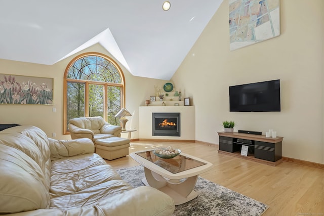 living room featuring vaulted ceiling, baseboards, a lit fireplace, and wood finished floors