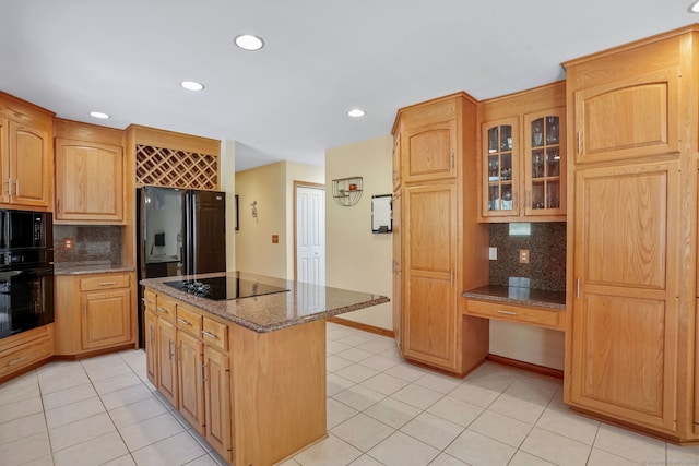 kitchen with decorative backsplash, glass insert cabinets, black appliances, and dark stone countertops