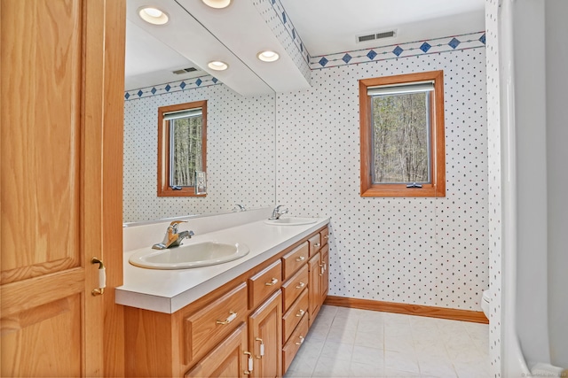 bathroom with visible vents, a sink, double vanity, and wallpapered walls