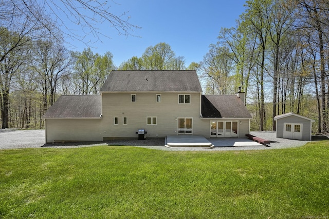 back of house with a shed, an outbuilding, a chimney, a patio area, and a lawn