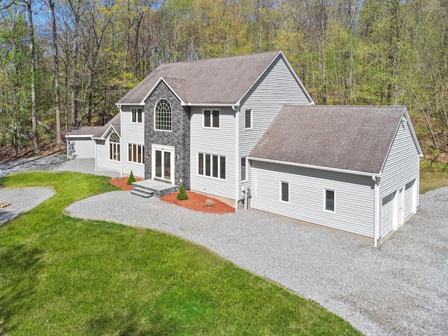 back of property featuring a shingled roof, stone siding, a lawn, an outdoor structure, and driveway