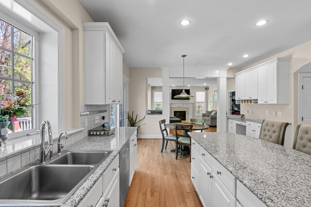 kitchen with a fireplace, light wood-type flooring, dishwasher, a sink, and white cabinets