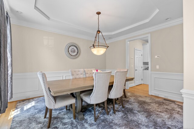 dining space featuring crown molding, a tray ceiling, wood finished floors, and a wainscoted wall