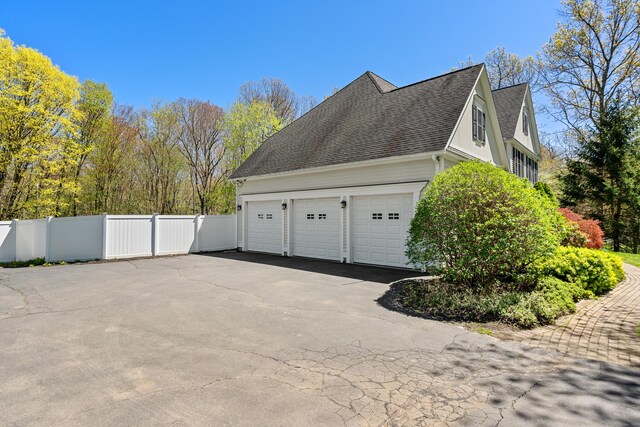 view of home's exterior featuring fence, a shingled roof, driveway, and a garage