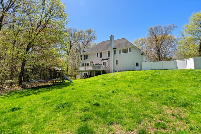 back of house featuring fence, a trampoline, a chimney, a playground, and a lawn