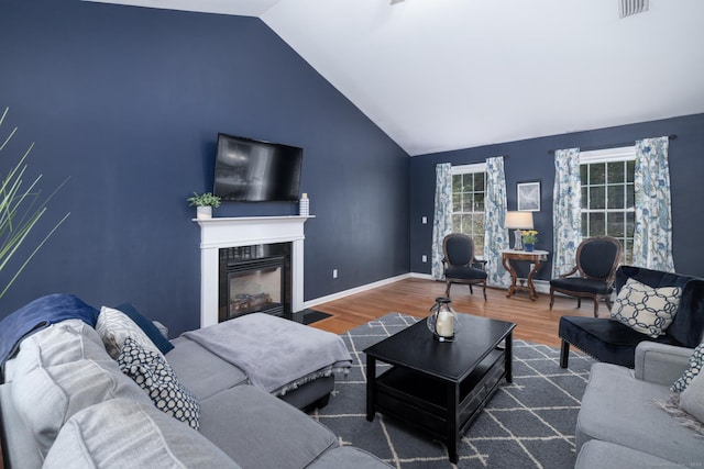 living room with visible vents, baseboards, a fireplace with flush hearth, wood finished floors, and vaulted ceiling