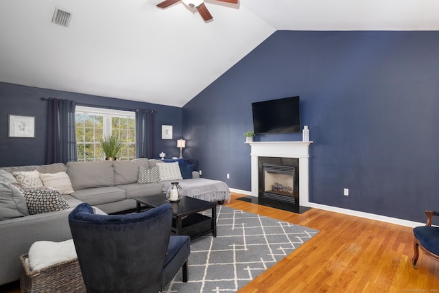 living room with a ceiling fan, visible vents, a fireplace with flush hearth, wood finished floors, and lofted ceiling