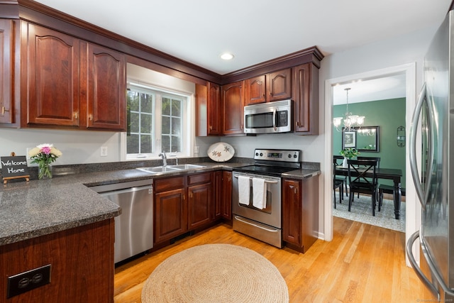 kitchen with dark countertops, a sink, a notable chandelier, stainless steel appliances, and light wood-style flooring