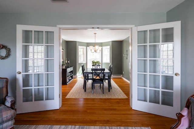 dining space featuring an inviting chandelier, a baseboard heating unit, wood finished floors, and visible vents