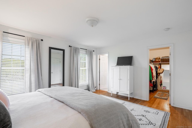 bedroom with a closet, light wood finished floors, baseboards, and a spacious closet