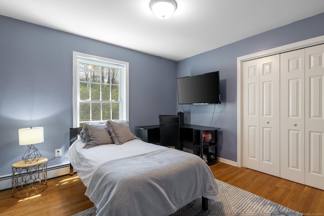 bedroom featuring baseboards, a baseboard heating unit, wood finished floors, and a closet
